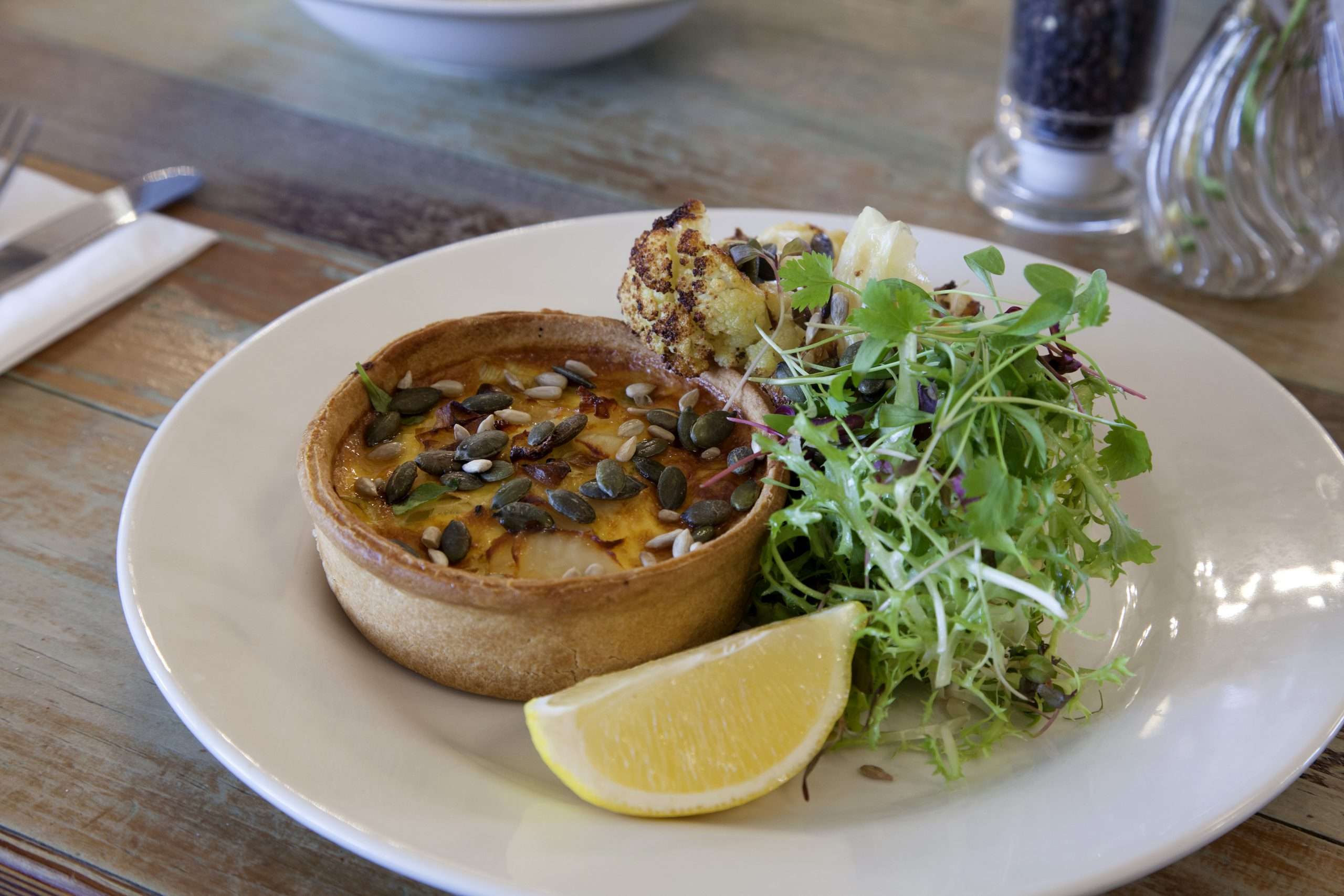 Homemade quiche with a green salad & a lemon wedge.